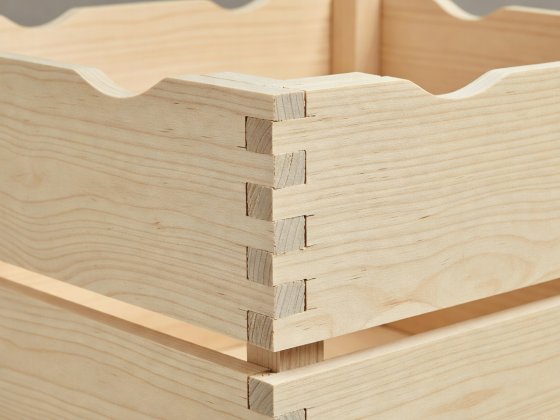 Close-up studio photograph of interlocking box finger joints on an unvarnished birch crate with rounded hand cut-outs
