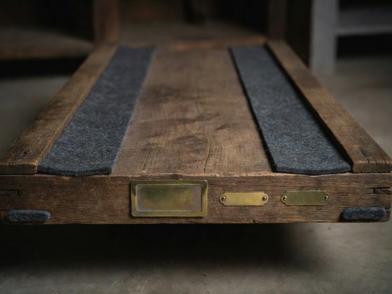Bottom edge of a wooden storage crate showing recessed wool felt runner strips and a clip-on brass card holder