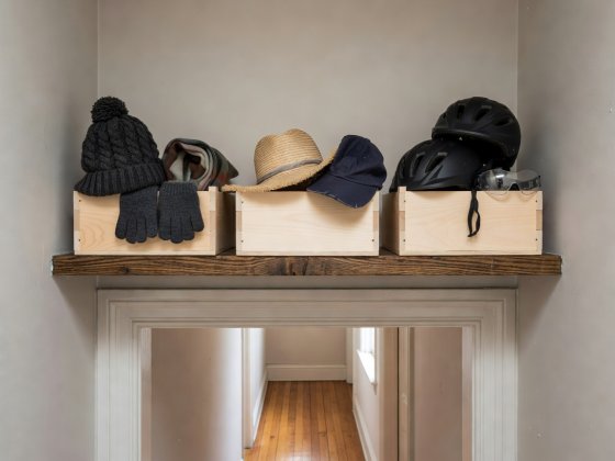 High hallway shelf above door architrave holding three numbered birch crates for seasonal hats and cycle helmets